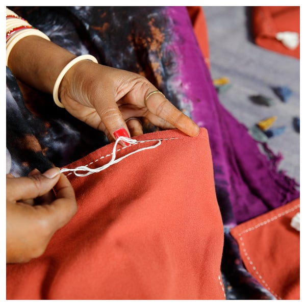 Hands embroidering orange fabric with white thread.