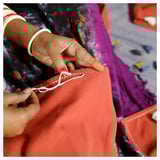 Hands embroidering orange fabric with white thread.