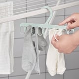Hand hangs socks on a mint-colored hanger with multiple loops.