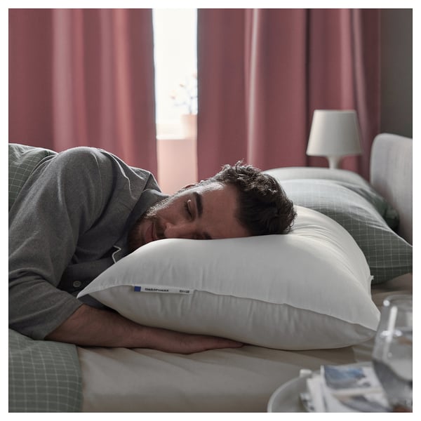 Man sleeps on white SMÅSPORRE pillow on green checkered bed, red curtains.