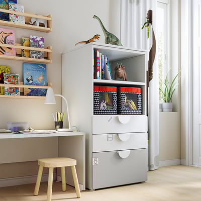 Childrens playroom with white SMÅSTAD bookcase and storage, wooden stool, desk, lamp, shelves with books, toys, and art supplies.