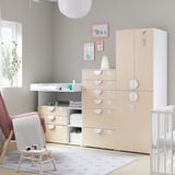 Modern nursery featuring light wood SMÅSTAD furniture set, changing table, and white crib. Colorful framed art and red chair add vibrancy.