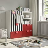 Childs room with gray-black striped wardrobe, shelves, red drawers, hanging cloth, white radiator, play mat, train tracks, and teddy bear.
