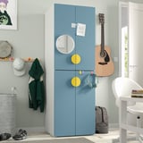Blue SMÅSTAD wardrobe with yellow handles, mirror, & soft-close hinges next to door. Surrounded by a chair, guitar, & wall art. Compact & spacious.