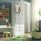 Childs room with white SMÅSTAD wardrobe, wooden shelves with books, and a green rug.