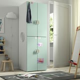 Green kids wardrobe with wooden handles near door, taller than nearby stool and rug.