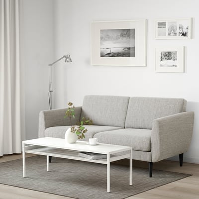Sofa in minimalist living room with photos, flowers, lamp.