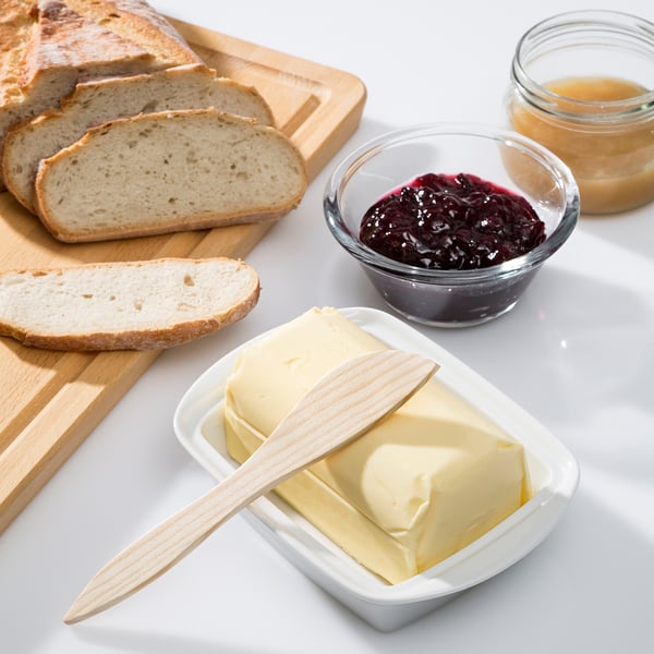 Bread slices near a butter dish with a knife and jams.