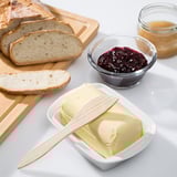 Bread slices near a butter dish with a knife and jams.