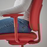 A person sits in a red office chair with armrests and height-adjustable seat, showcasing its ergonomic design.