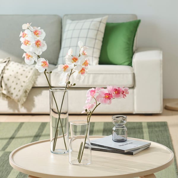 Modern living room with white sofa, colorful pillows, coffee table with books, candles, and orchids.