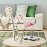 Modern living room with white sofa, colorful pillows, coffee table with books, candles, and orchids.