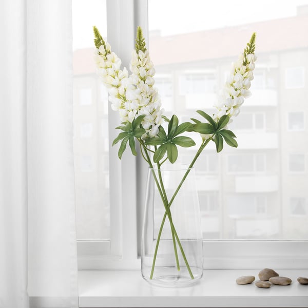 Clear vase with white flowers on windowsill, reflecting sunlight.