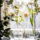 Clear glass vases with light yellow and white artificial flowers on a windowsill.