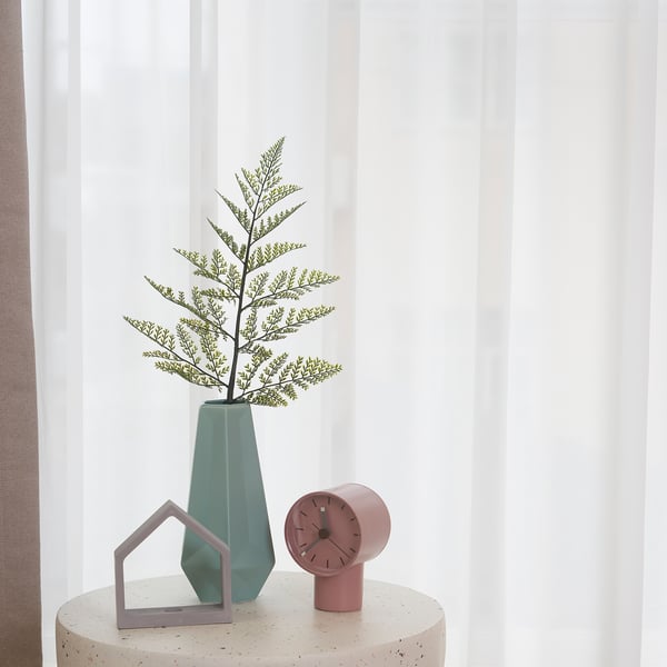 A decorative green vase with adjustable artificial plant sits on a table, next to a pink clock.
