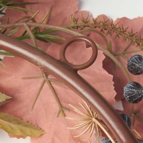 Brown wreath with dried flowers and dark berries, up close, on pink textile.
