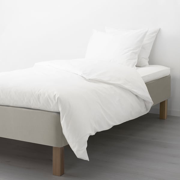 A neatly made bed with a white mattress and bedding on a wooden base, supported by visible wooden legs.