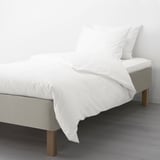 A neatly made bed with a white mattress and bedding on a wooden base, supported by visible wooden legs.