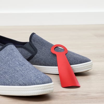 Blue sneakers with a red shoehorn inserted, on wooden floor.