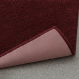 Burgundy bath mat with pivotable corner showing latex backing for secure grip on smooth surfaces.
