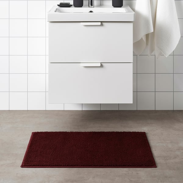 Red rectangular SÖDERSJÖN bath mat with white cabinet and sink.