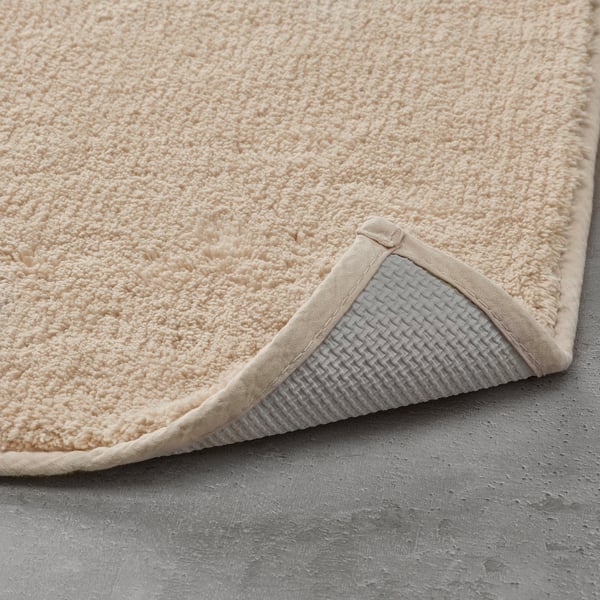 Light beige bath mat with textured cotton surface and non-slip latex backing.