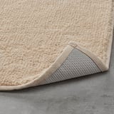 Light beige bath mat with textured cotton surface and non-slip latex backing.
