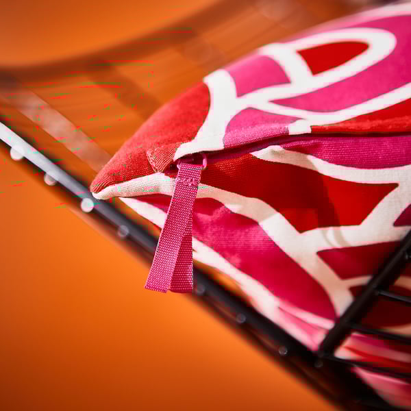 Pink-red abstract-patterned cushion cover with zipper on black stand.