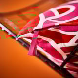 Pink-red abstract-patterned cushion cover with zipper on black stand.