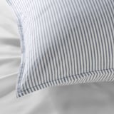 Blue and white striped pillow on white bedding. Close-up detailed stitching and soft fabric texture.