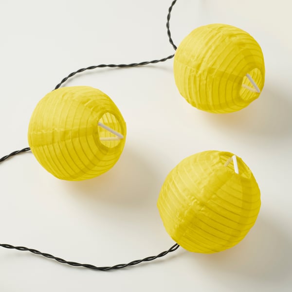 Yellow spherical lanterns hang in a row, connected by black cord, emitting a warm glow. Ideal for indoor/outdoor use, creating a cozy atmosphere.