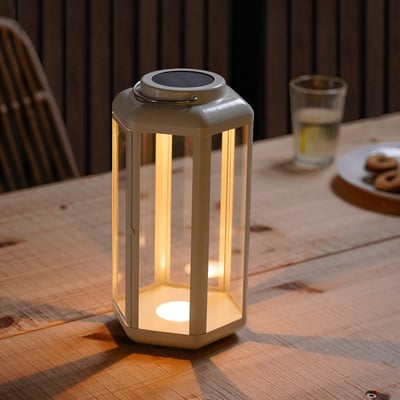 Small SOLVINDEN lantern on wooden table, emitting soft light, next to a glass and cookies.