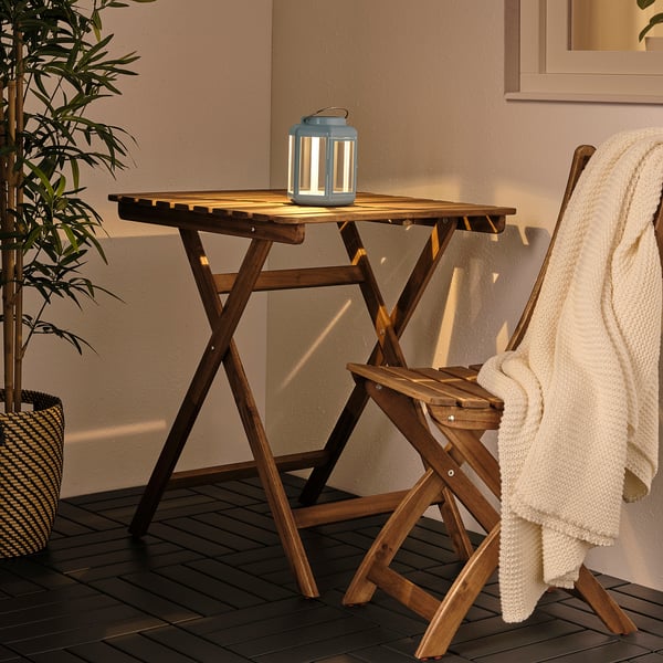 Small SOLVINDEN blue solar lamp sits on wooden table beside white blanket, next to a plant.