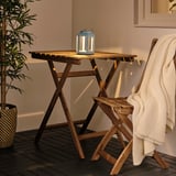 Small SOLVINDEN blue solar lamp sits on wooden table beside white blanket, next to a plant.