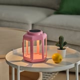 Bright pink solar lantern on a white table, emitting warm light, beside a lemon and a small cactus.