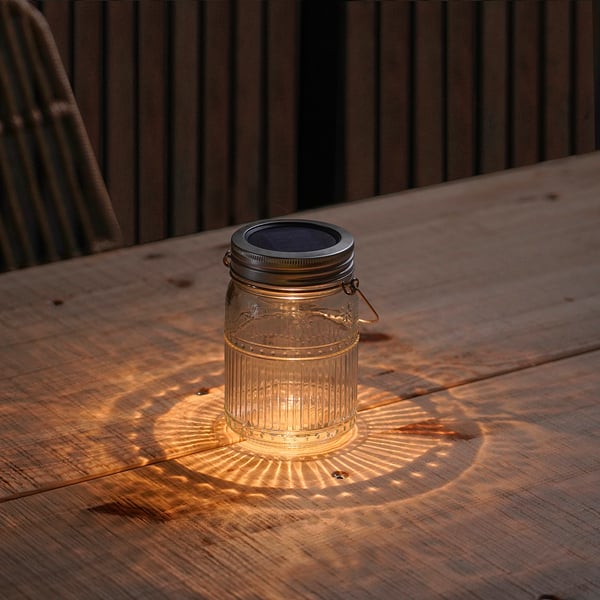 Small SOLVINDEN lantern on wooden table casting lit pattern, using solar power.