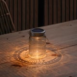 Small SOLVINDEN lantern on wooden table casting lit pattern, using solar power.