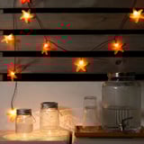 Orange star lights above jars on wooden shelf, creating warm glow.