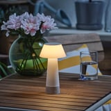 Modern led lamp on wooden table, illuminated, beside clear glass vase with pink flowers and water glass.
