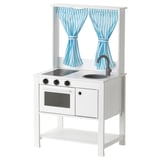 White play kitchen set with striped blue curtains, sink, stove, oven, and shelf.