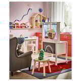 Playroom with SPISIG play kitchen in white, red, and blue. Stove, sink, shelf, and curtain. Accompanied by a grey chair and small wooden stool.