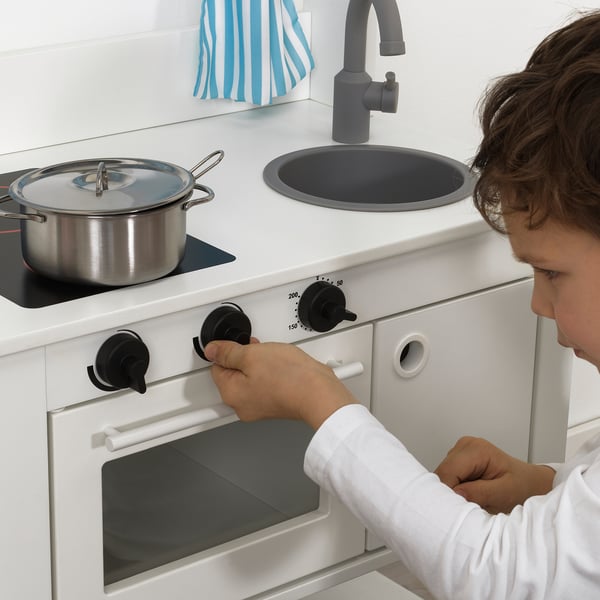 A child plays with a toy kitchen, turning stove knobs. Its realistic with clicking controls and a sink, promoting imaginative role-play.