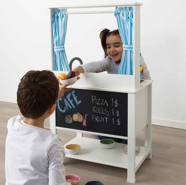 Children playing with play kitchen, one serving, blackboard menu, curtains.