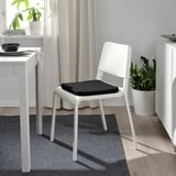 Black STAGGSTARR cushion on white chair near desk, with green plants.