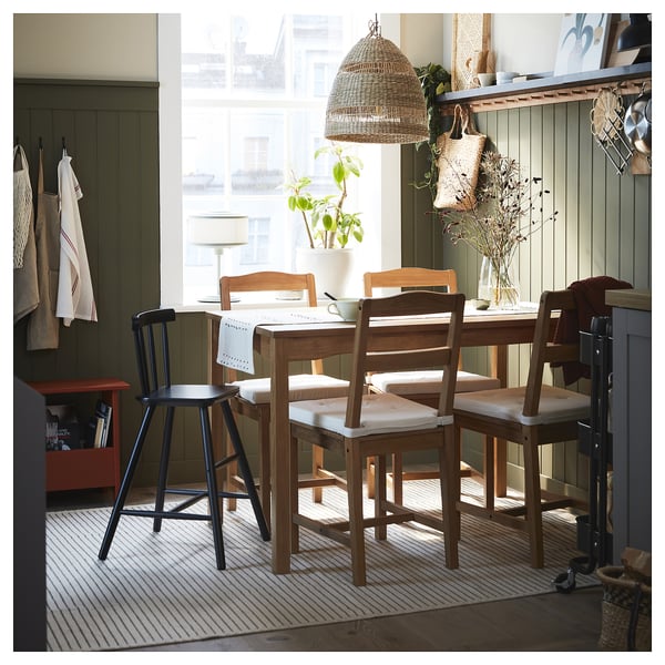 Cozy dining area with wooden table, chairs, striped rug, window, plants, basket, lamp.