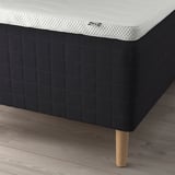 Close-up of a white mattress on black bed base with wooden legs by IKEA.
