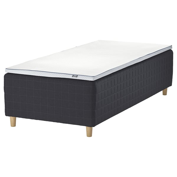 An IKEA STAVANGER bed in dark grey with a white mattress. It wooden legs and a quilted design.