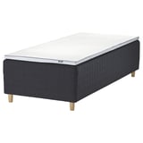 An IKEA STAVANGER bed in dark grey with a white mattress. It wooden legs and a quilted design.