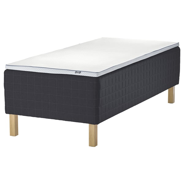 Black ikea STAVANGER bed with dark grey quilted frame and light wooden legs. Mattress has white and grey textured surface for comfort and support.