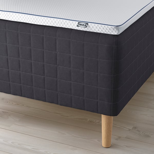 A close-up of an ikea mattress on a bed with wooden legs, showing its textured sides and comfortable design.